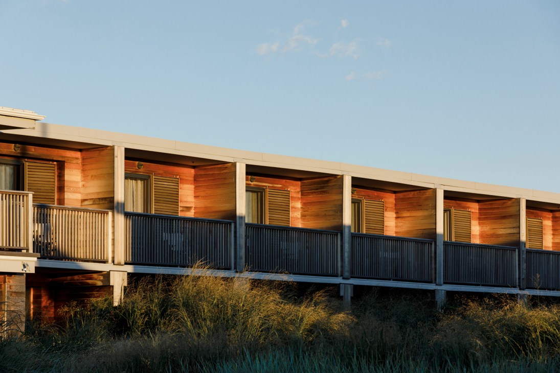 Modern wooden hotel building with horizontal slat railings elevated on stilts among coastal dune grass