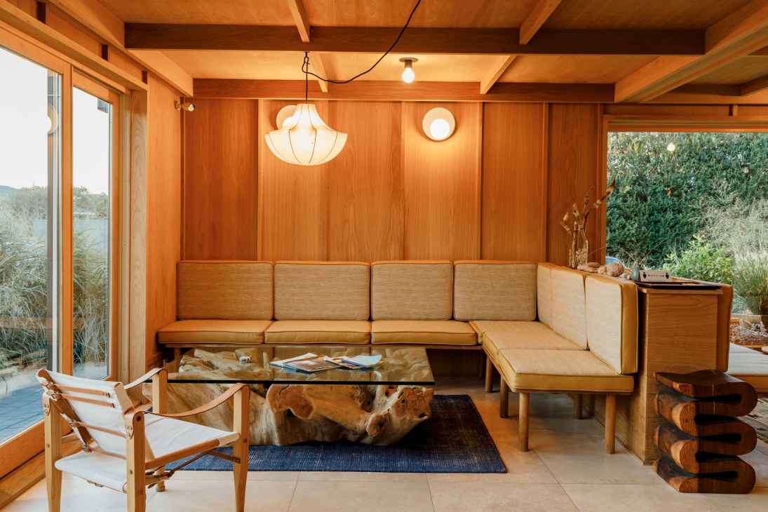 Modern living room with wood-paneled walls, built-in sectional seating, and large windows overlooking greenery