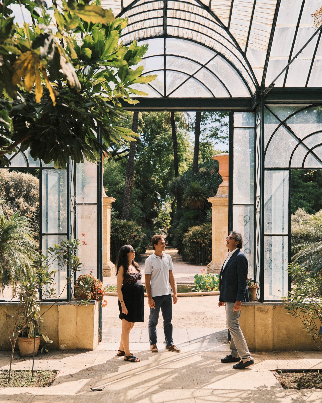 Three people standing under an arched glass conservatory structure in Palermo's botanical gardens