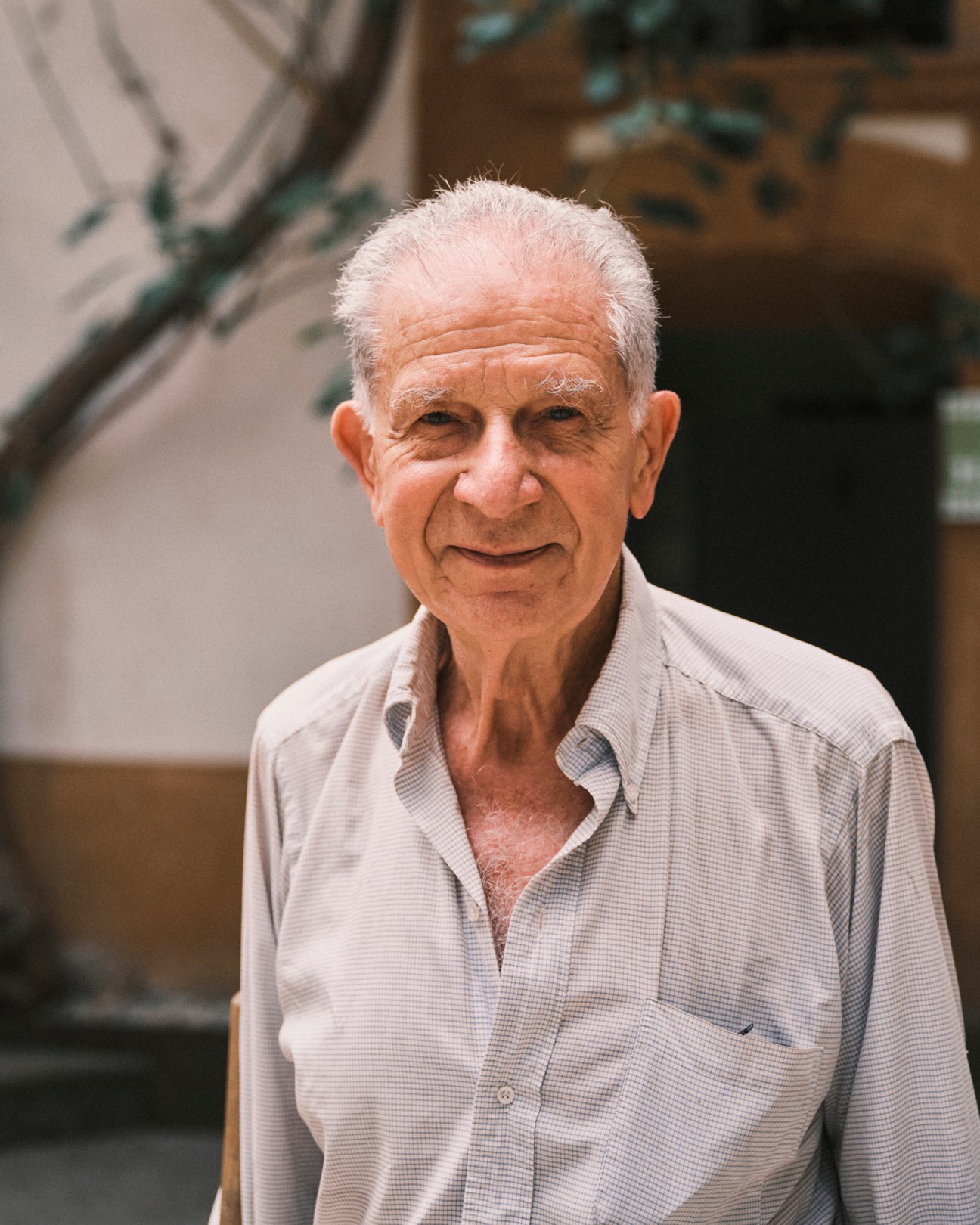 Elderly man with white hair and checkered shirt smiling at camera in front of building