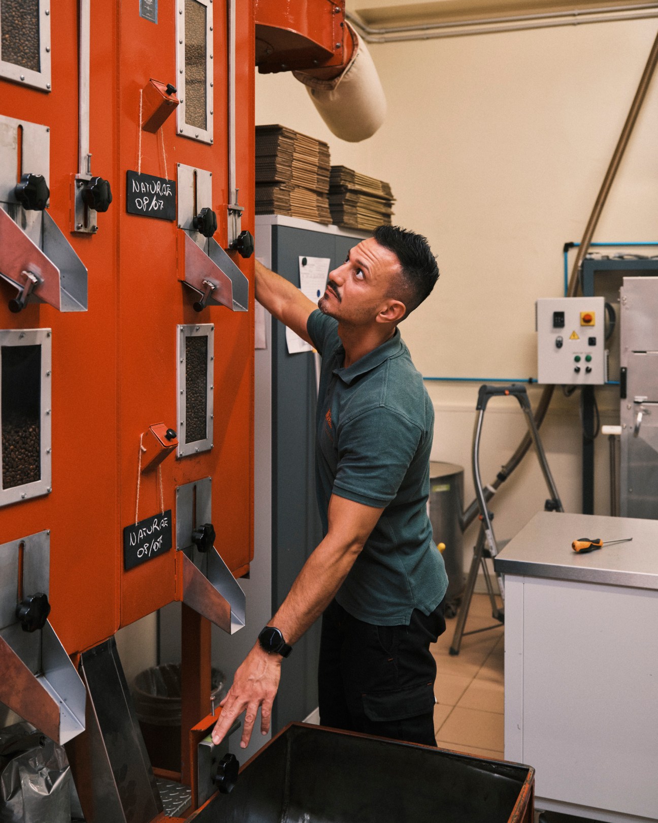 A man in a green polo shirt operates orange coffee roasting equipment at Morettino's headquarters facility