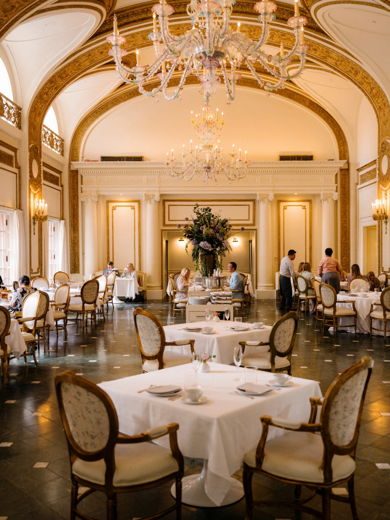 Elegant dining room at The Adolphus hotel with crystal chandeliers, arched ceiling, and white tablecloth tables