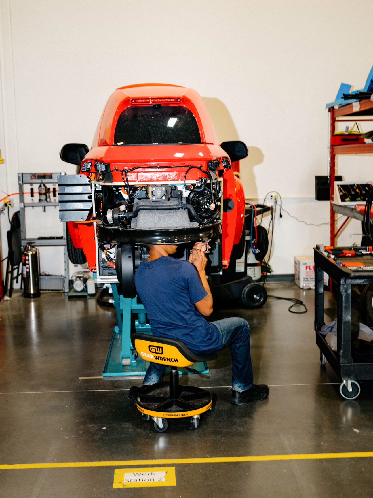 Engineer working on electric vehicle assembly in factory setting with vehicle on lift