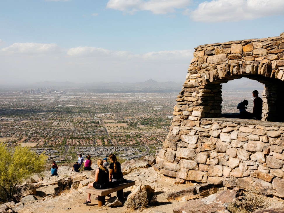 Stone ruins with arched opening overlooking Phoenix valley sprawl with desert mountains in background
