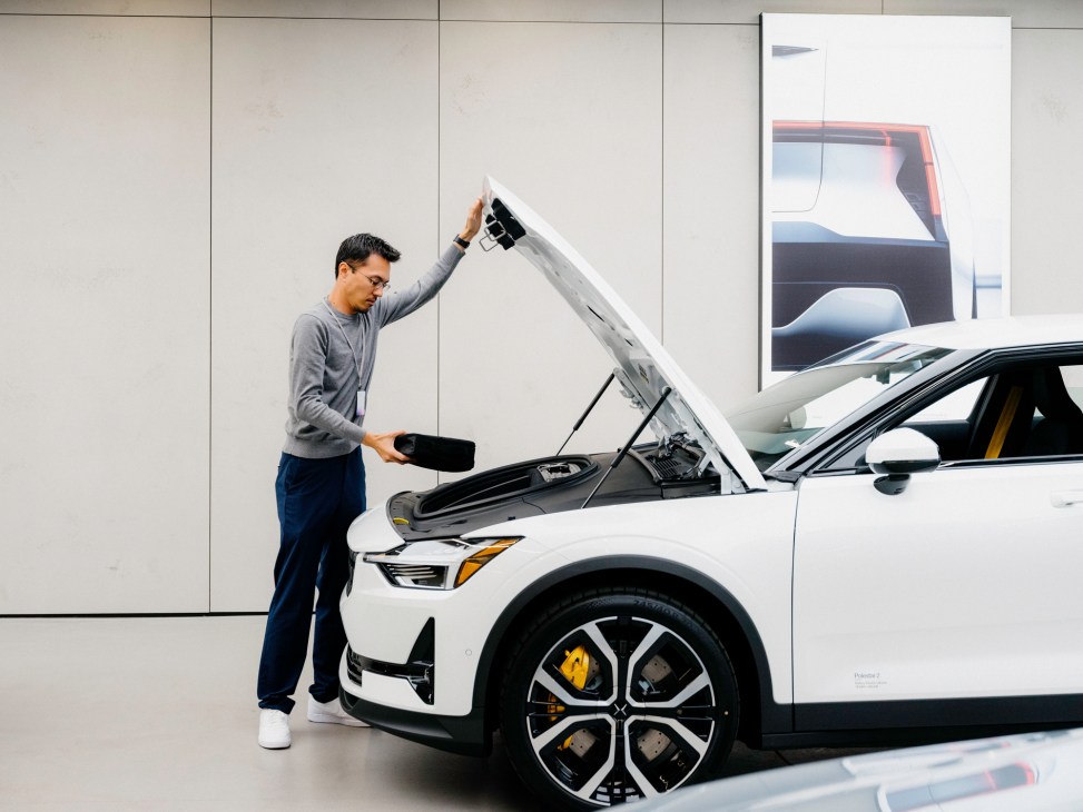 Man examining white electric car with open hood in modern Polestar showroom