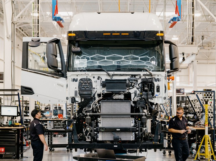 Electric truck assembly line in modern factory with workers and lifting equipment