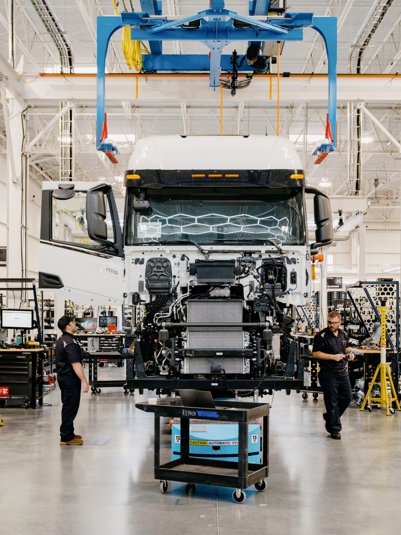 Electric truck assembly line in modern factory with workers and lifting equipment
