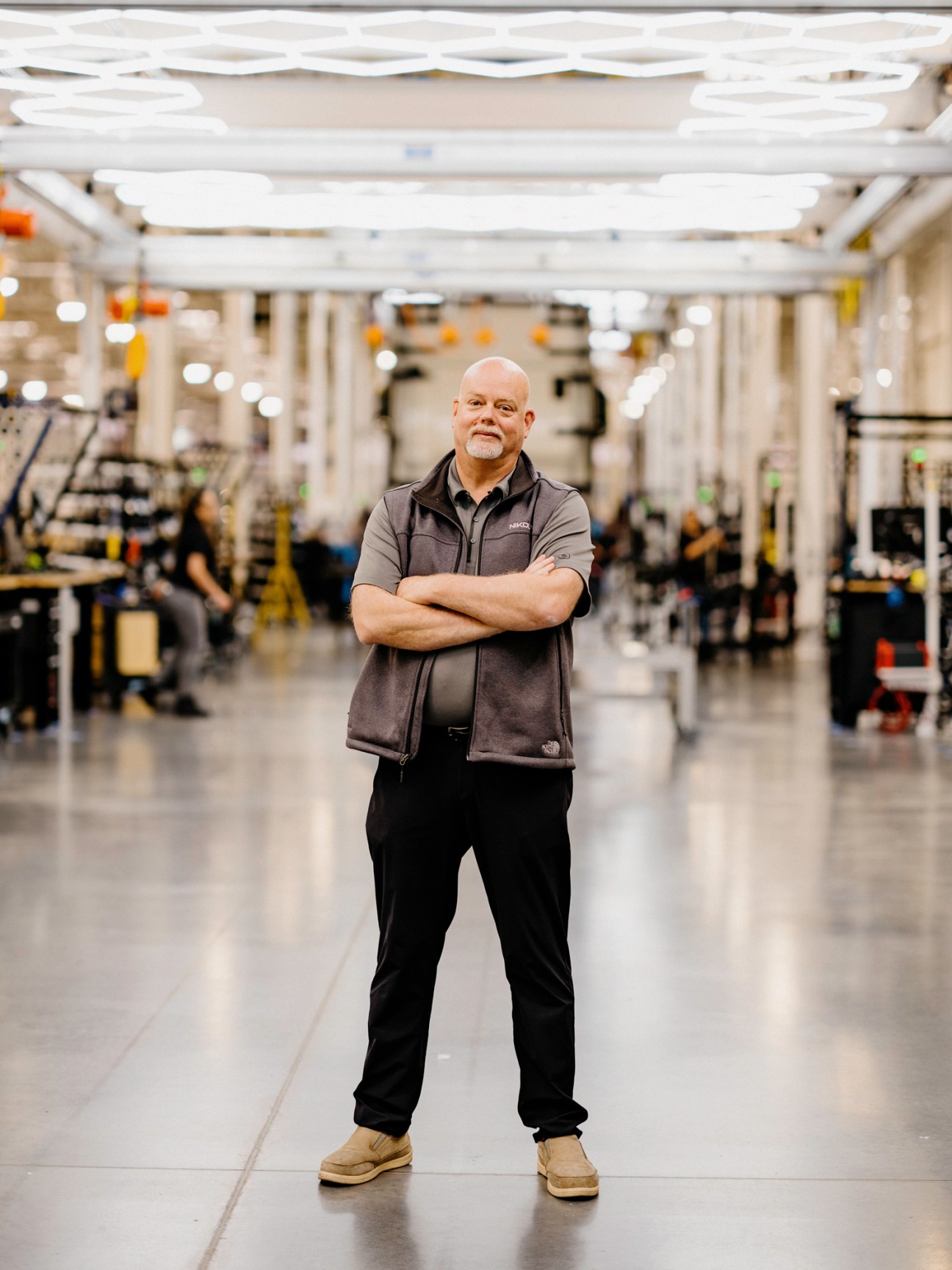 Mark Duchesne standing with crossed arms in a modern manufacturing facility with white industrial equipment