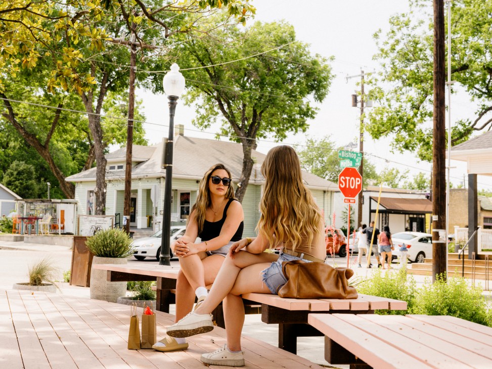 Two women sitting on wooden bench at outdoor seating area in Bishop Arts District