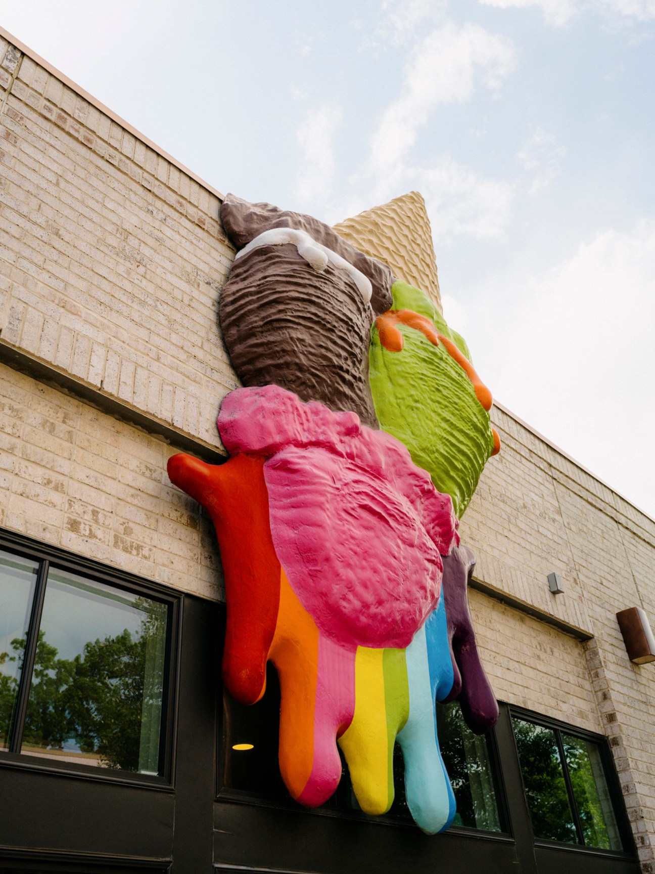 Large colorful ice cream cone sculpture mounted on brick building exterior