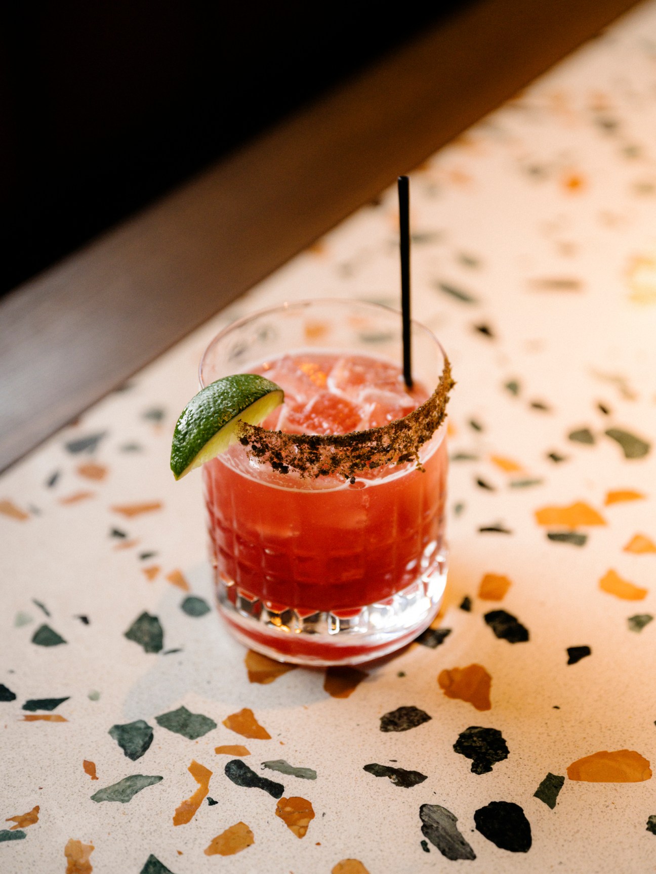 Red cocktail with lime garnish and spiced rim on terrazzo surface