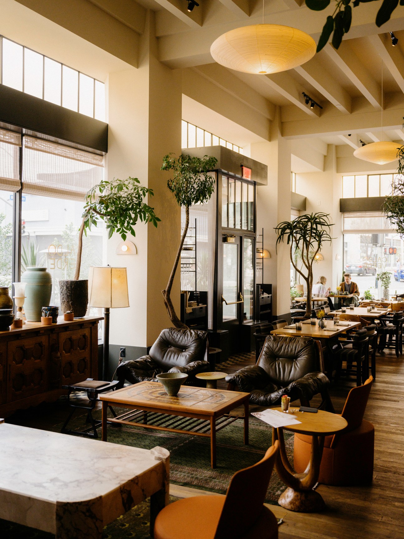 Interior view of Caldo Verde restaurant showing seating area with leather chairs, wooden tables, plants and pendant lighting