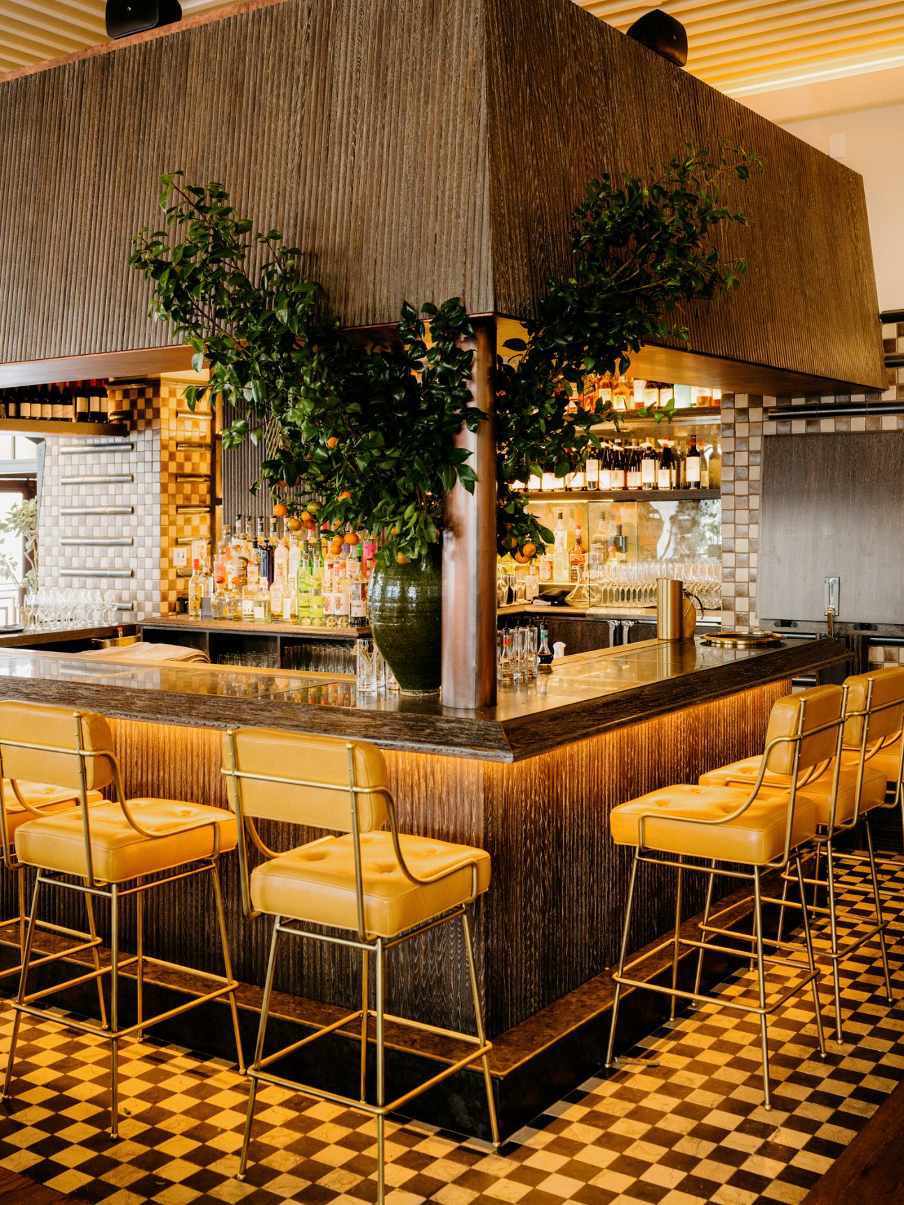 Bar area at Caldo Verde restaurant with golden bar stools, checkered floor, and overhead range hood