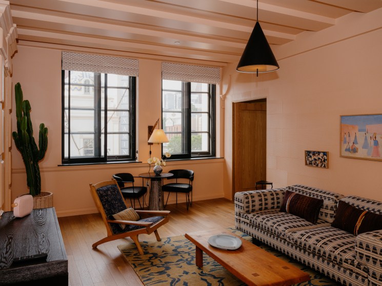 Hotel room interior with plaid sofa, wooden coffee table, black pendant lamp and large windows overlooking downtown
