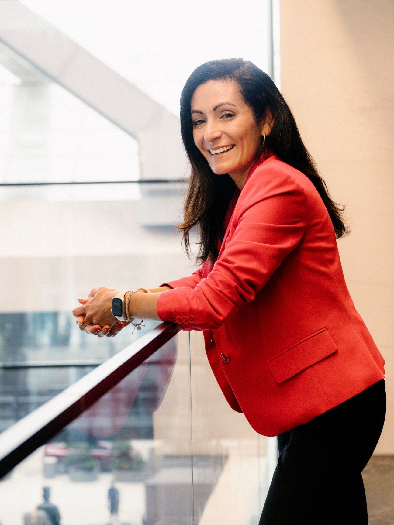 Professional woman in red blazer smiling while standing at office balcony railing