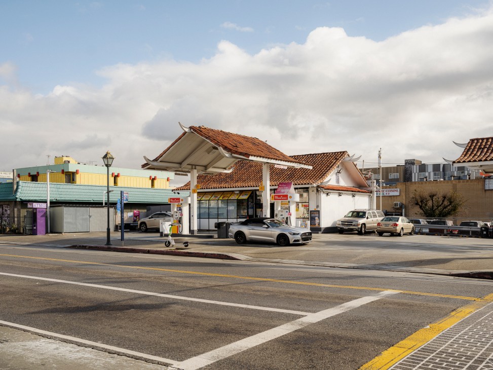 Gas station with distinctive red tile roof and white walls featuring fuel pumps under covered canopy