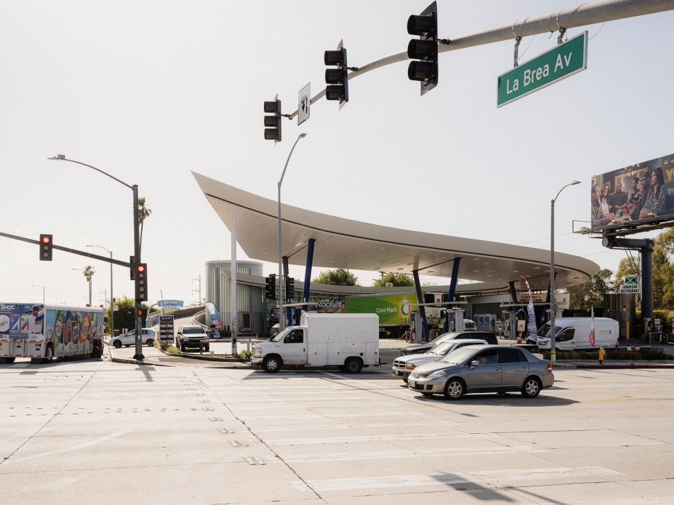 Modern gas station with curved white canopy and multiple fuel pumps at busy intersection