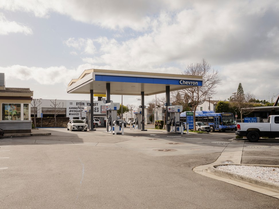 Chevron gas station with white canopy and blue signage, vehicles at pumps including a blue bus