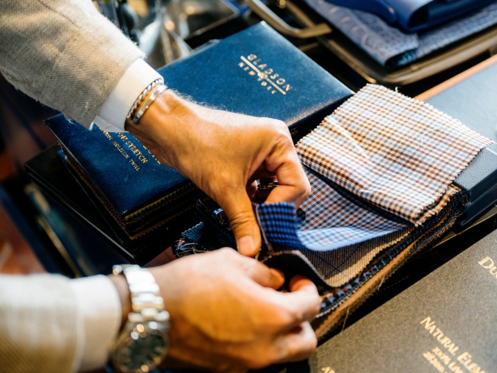 Hands selecting fabric swatches from organized sample books at Hadleigh's bespoke tailoring shop