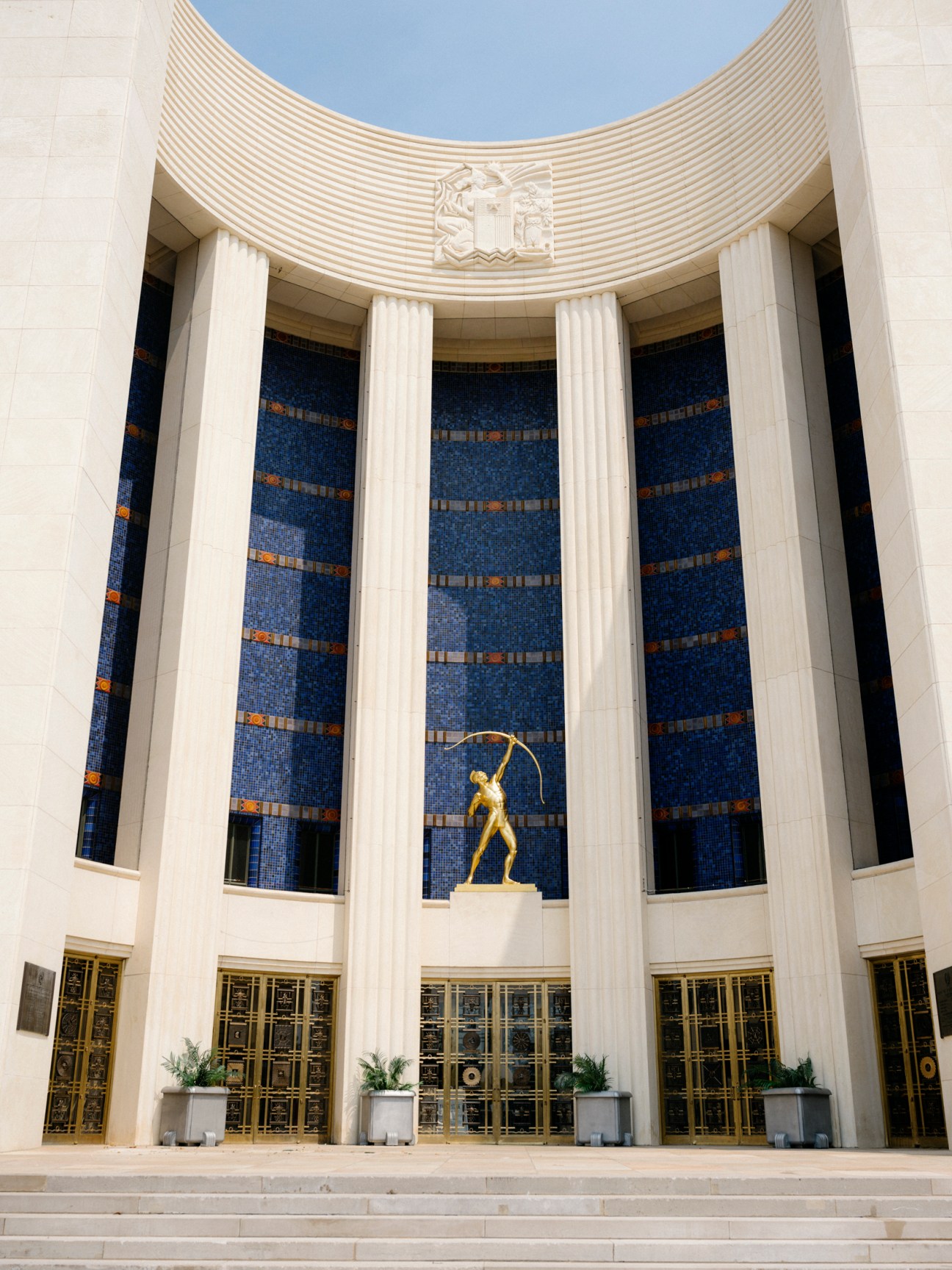 Art deco building with curved facade, columns, blue mosaic walls and golden statue at Fair Park Dallas