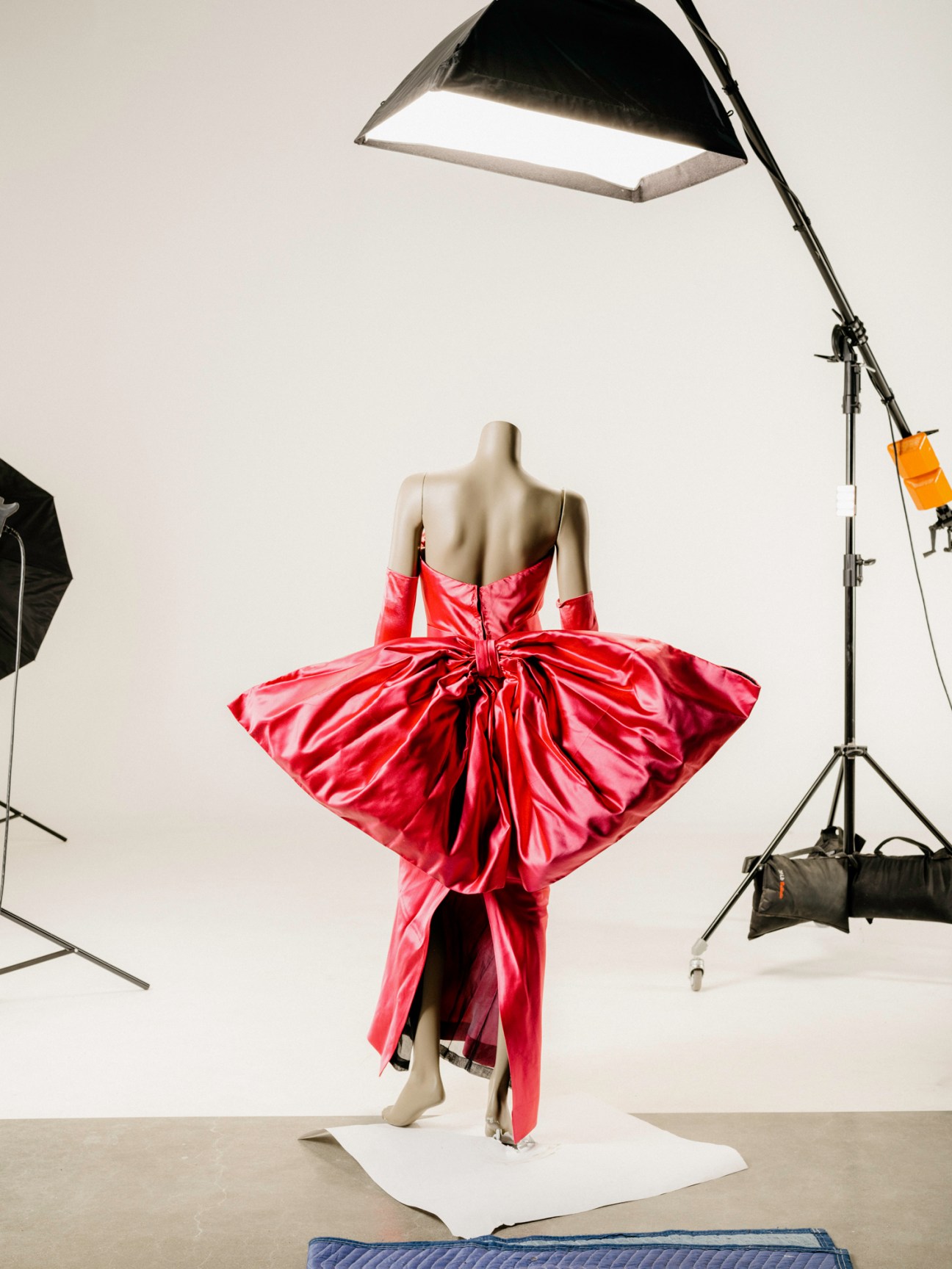 A mannequin wearing an elaborate red leather dress with dramatic draping and ruffled detailing in a photo studio
