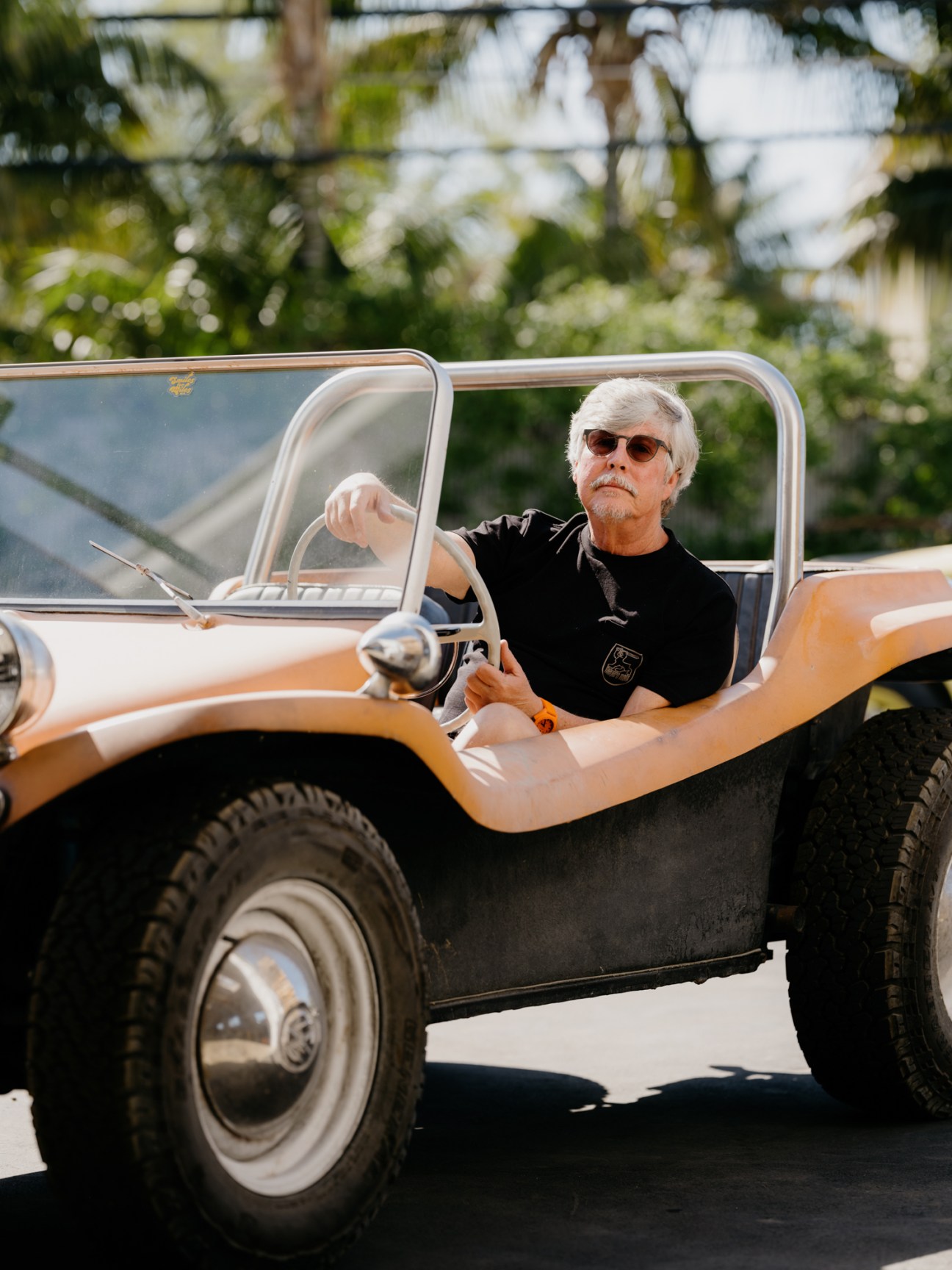 Man with gray hair and sunglasses sitting in vintage orange and white convertible vehicle