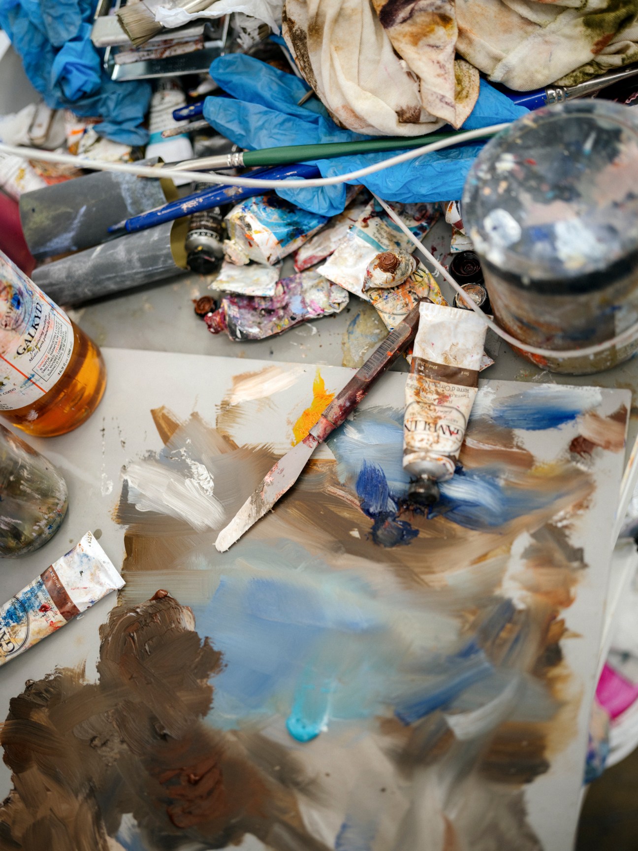 Paint tubes, brushes, and artist palettes covered in colorful oil paints scattered on a work surface