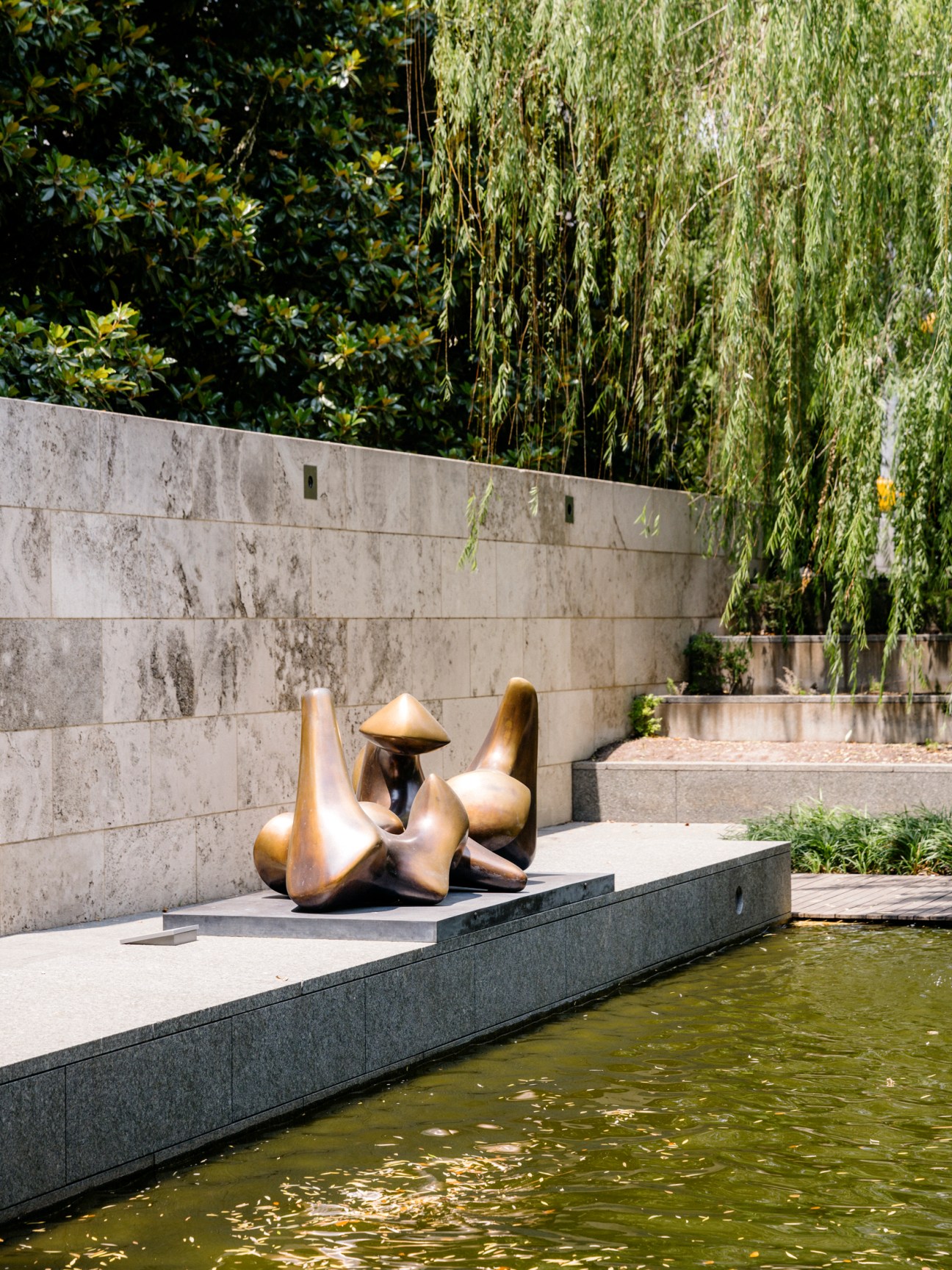 Bronze sculpture by water feature at Nasher Sculpture Center garden with stone wall and greenery