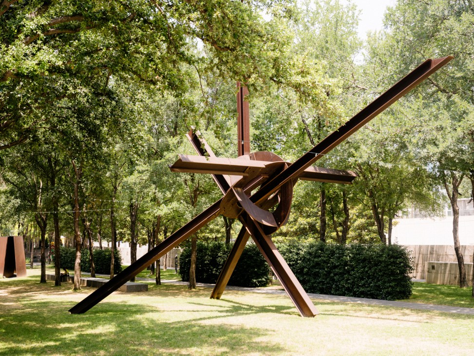 Large abstract bronze sculpture with intersecting angular beams in outdoor garden setting at Nasher Sculpture Center