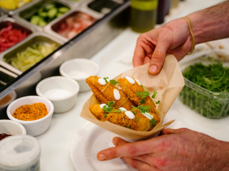 Golden fried cauliflower tacos with white sauce and herbs served in wooden boat at National Anthem restaurant
