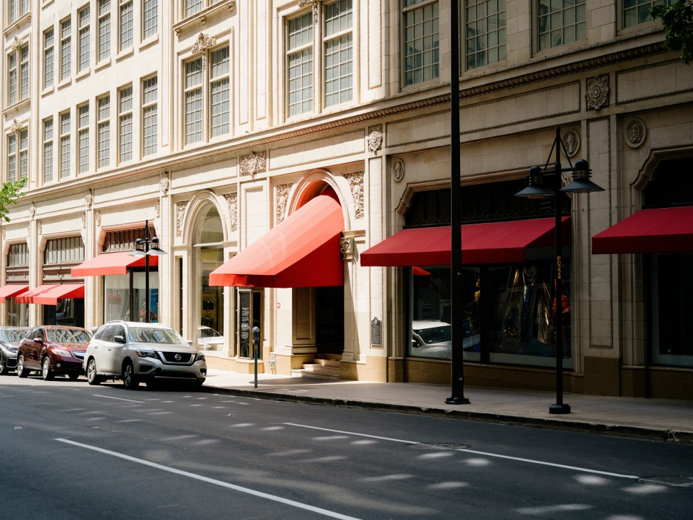 Historic Neiman Marcus flagship store building with white terracotta facade, red awnings, and parked cars on Main Street
