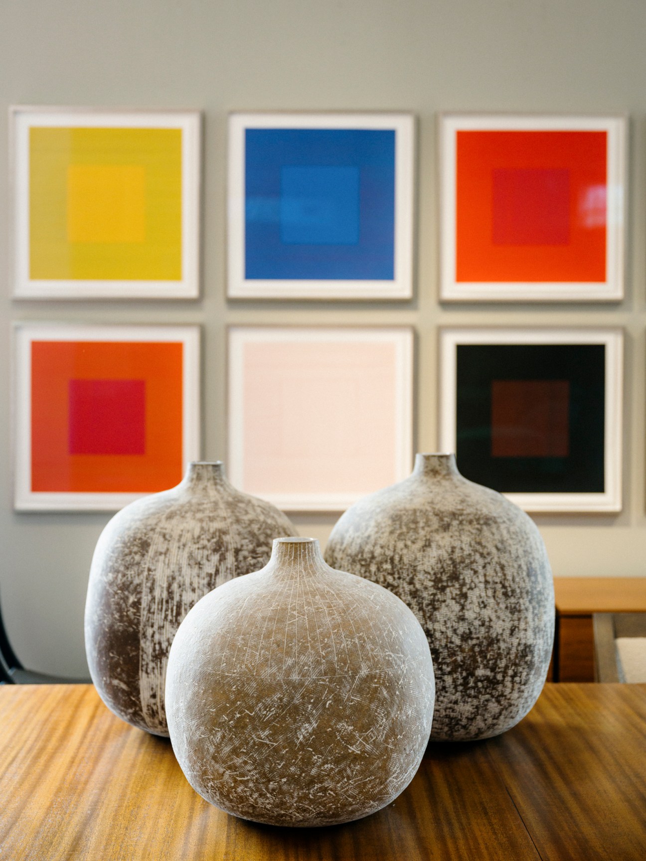 Three ceramic vases with weathered white and gray finishes on wooden surface with colorful framed artworks