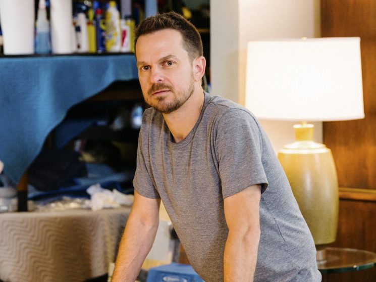Man in gray shirt standing at table with papers in furniture showroom with mid-century pieces
