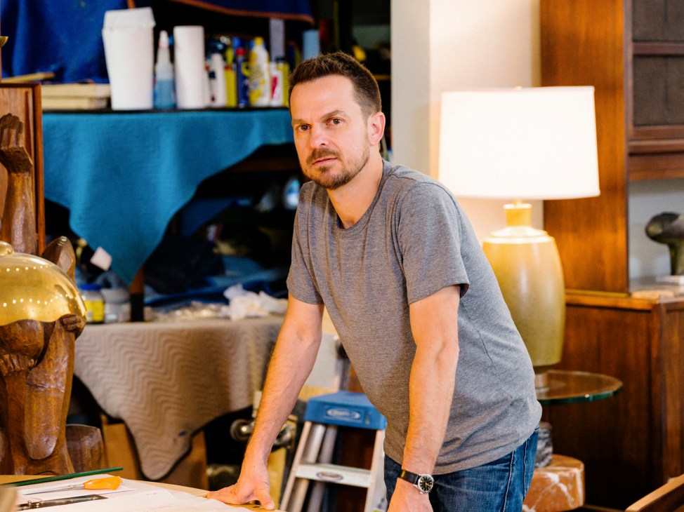 Man in gray shirt standing at table with papers in furniture showroom with mid-century pieces