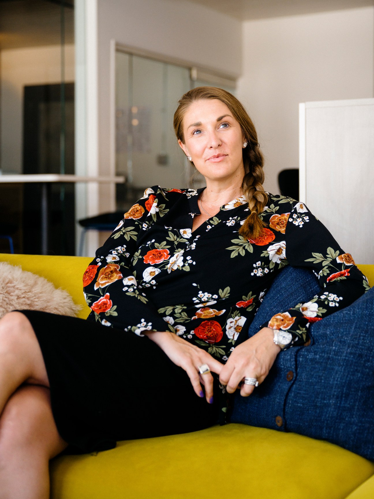 Woman in floral blouse sitting on yellow sofa in modern office interior