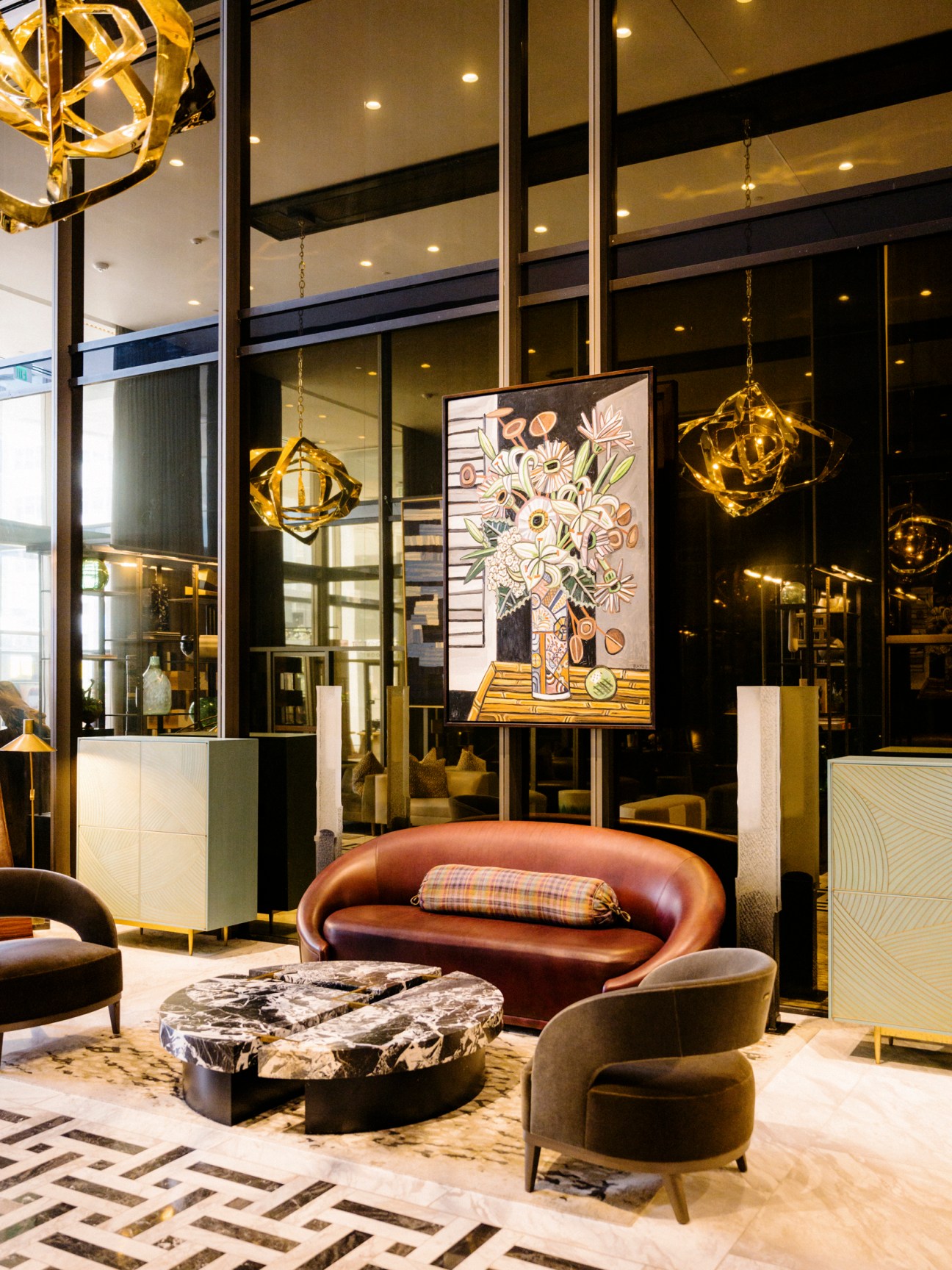 Modern hotel lobby with curved leather seating, marble coffee table, geometric pendant lights and colorful artwork