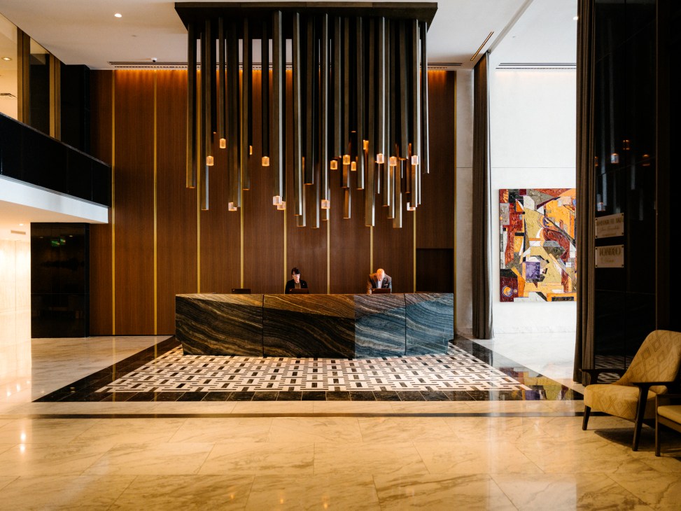 Modern hotel lobby with dramatic hanging light installation, marble reception desk, and warm wood paneling