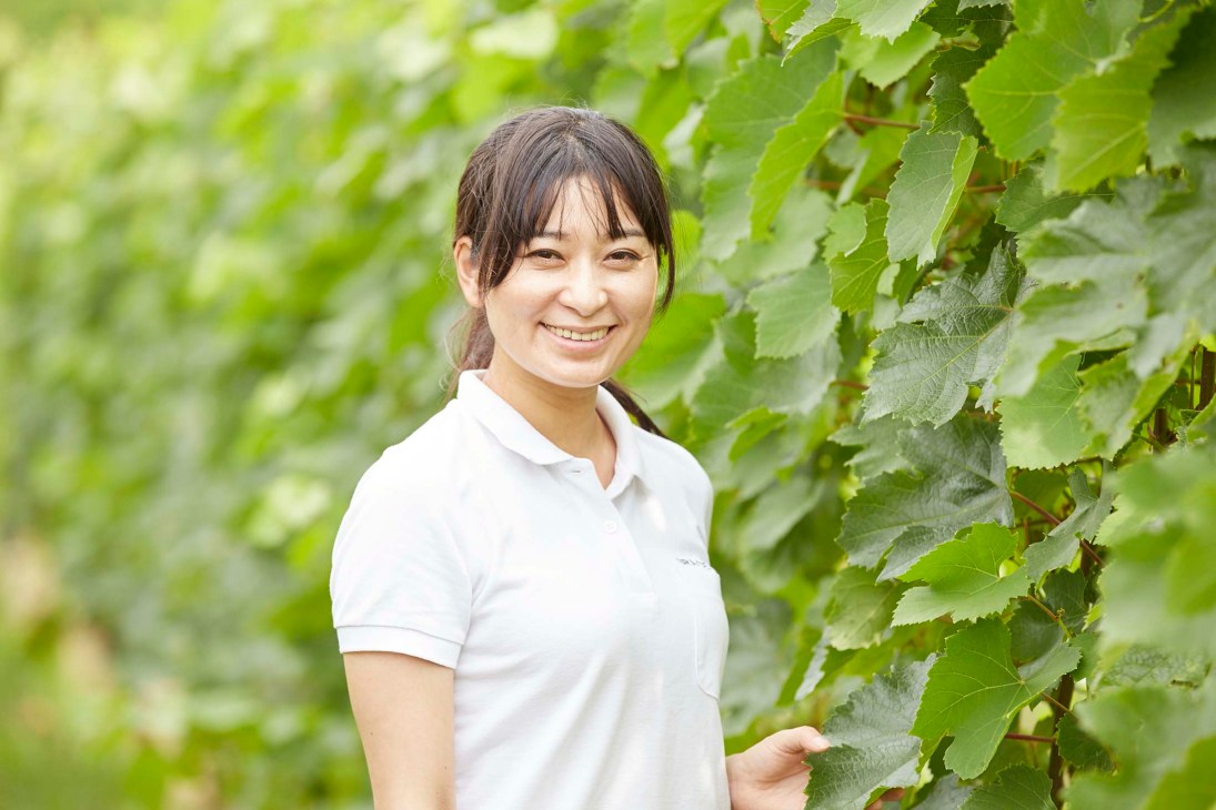 Woman in white polo shirt smiling among green foliage
