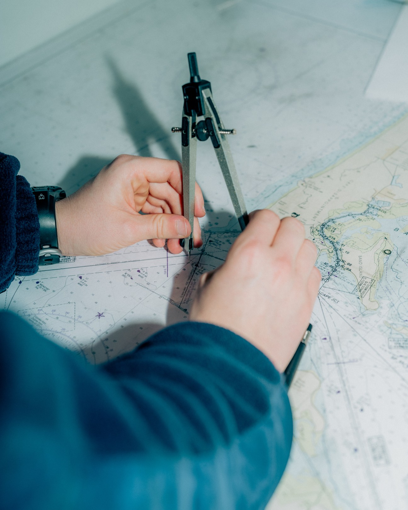 Hands using a compass to navigate on nautical charts and maps