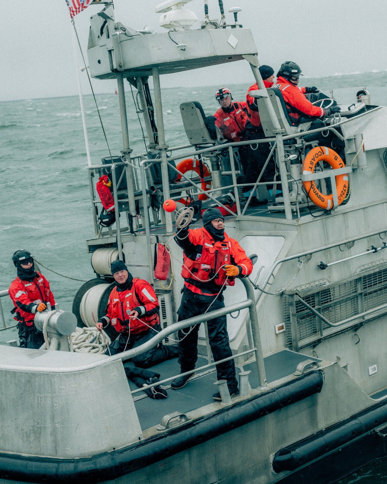 Coast Guard personnel in red protective gear handling ropes during training exercise on rescue boat