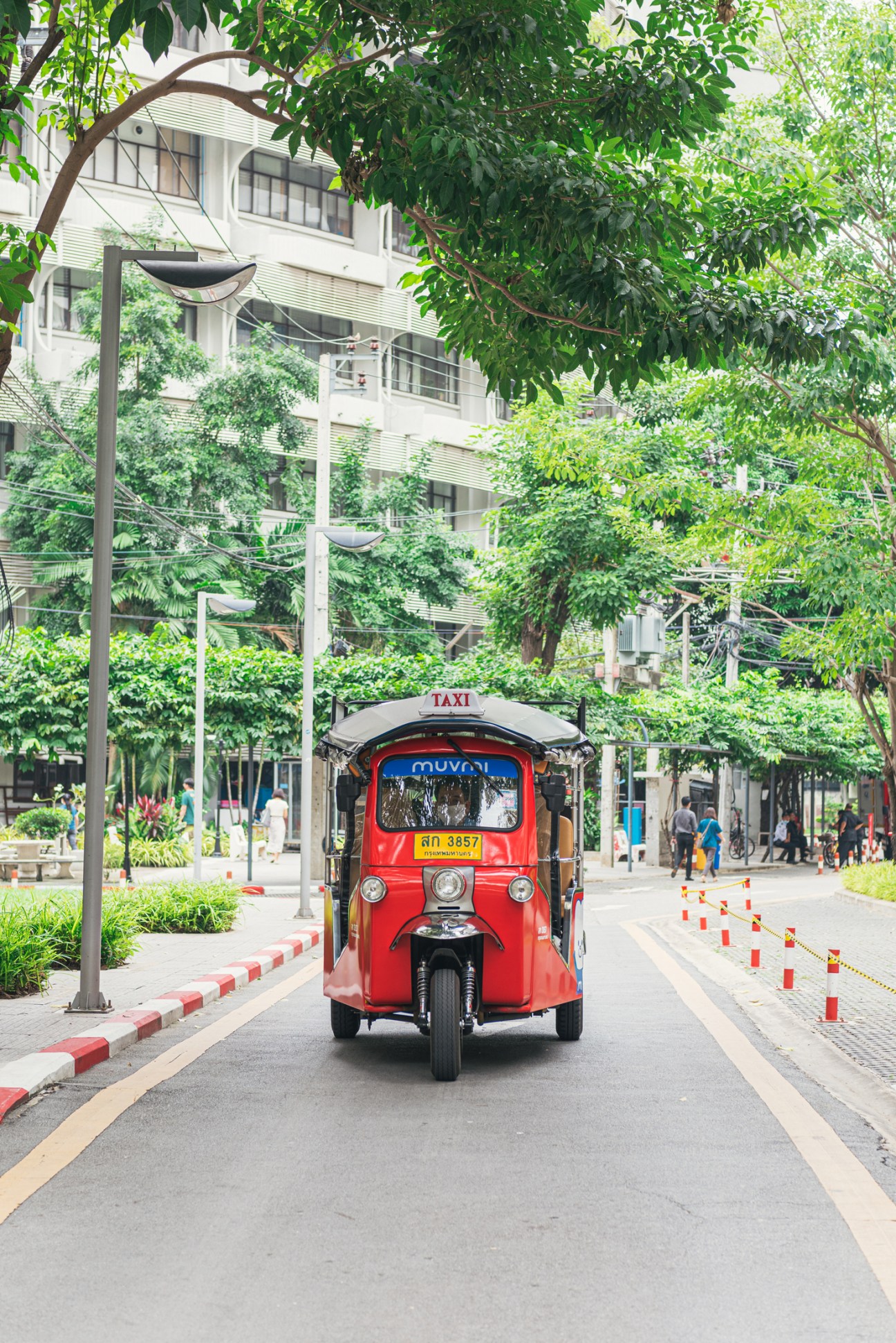 Red three-wheeled electric tuk-tuk taxi on a tree-lined street in Bangkok