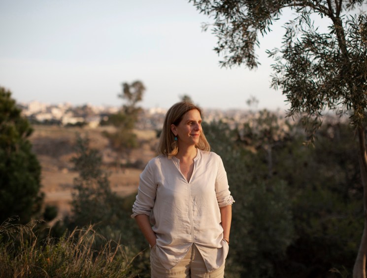 Woman in white shirt standing outdoors with hills and vegetation in background during golden hour