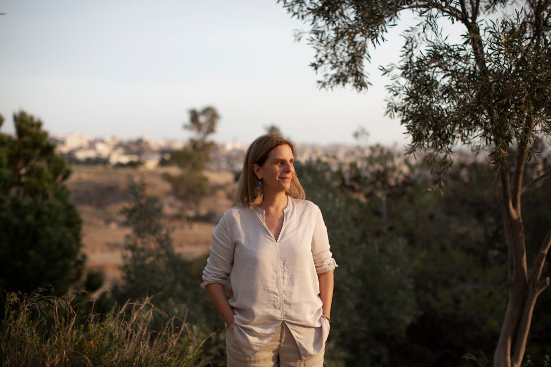 Woman in white shirt standing outdoors with hills and vegetation in background during golden hour