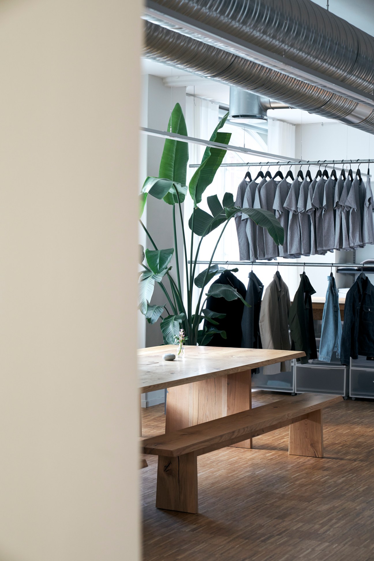 Interior view of Asket's Stockholm boutique with wooden display table, clothing racks, and green plants.