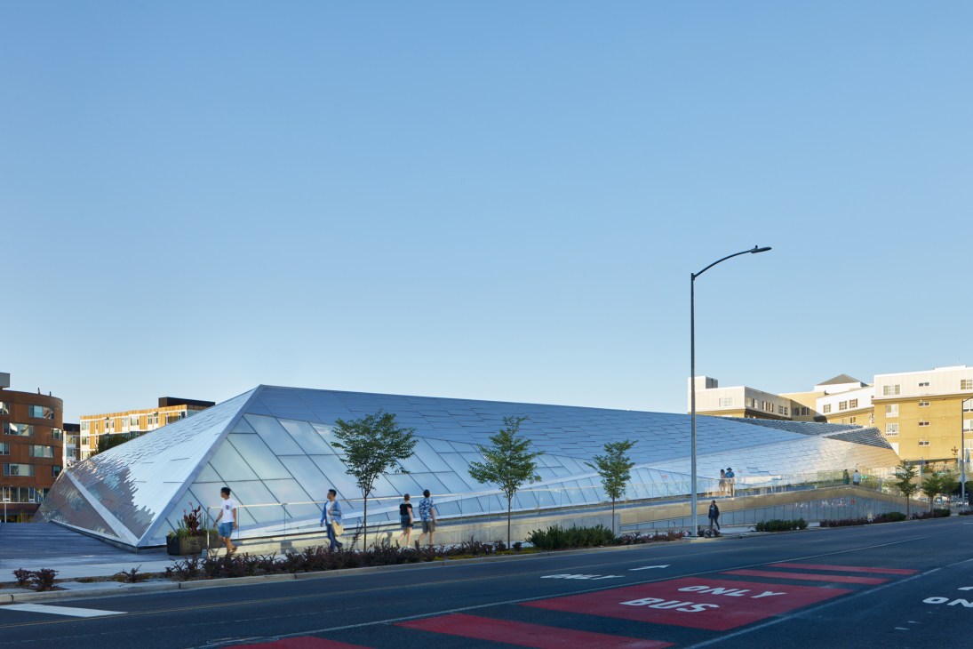 Modern angular building with geometric glass facade and people walking on elevated walkway in urban setting