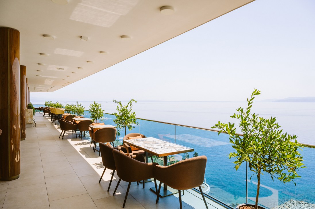 Modern restaurant terrace with brown chairs and marble tables overlooking blue Adriatic Sea from covered balcony