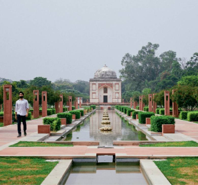 Person walking through formal garden with geometric water channels leading to domed Mughal monument structure