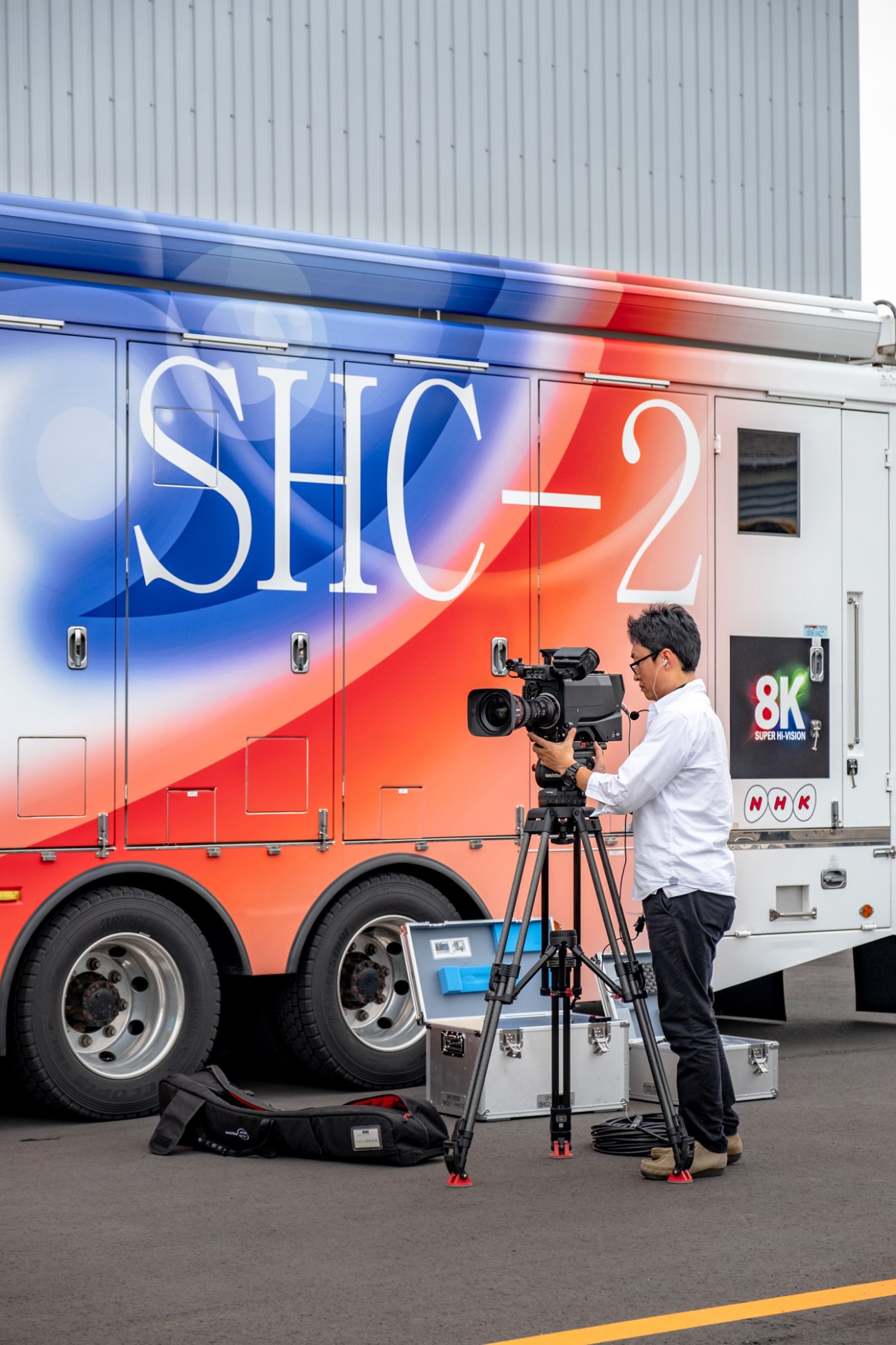 NHK cameraman operating professional video equipment on tripod beside colorful broadcast truck