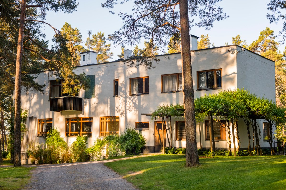 Villa Mairea exterior with white limestone and wood architecture surrounded by tall coniferous trees