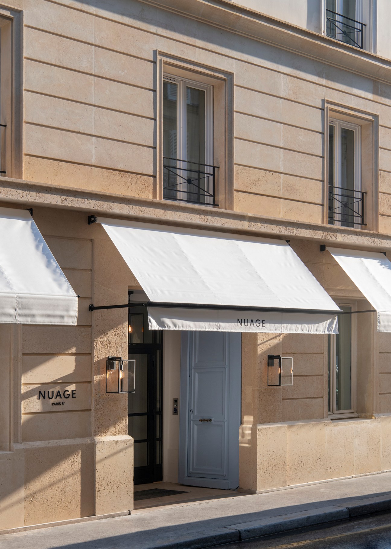 Hotel Nuage Paris facade with beige stone architecture, white awnings, and blue entrance door